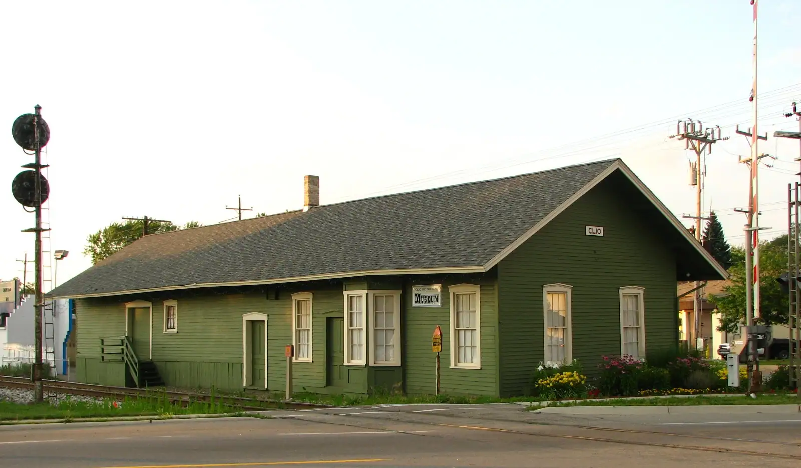 A restored green railroad depot with flower beds