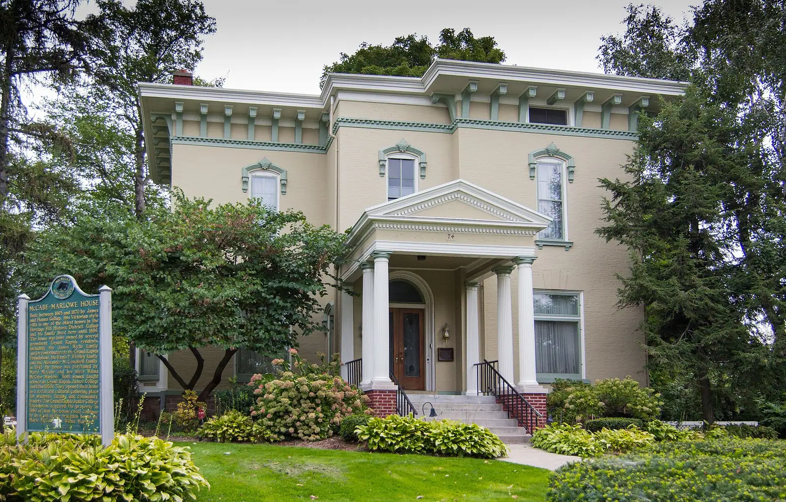 A cream-colored historic house with a columned porch and mature trees