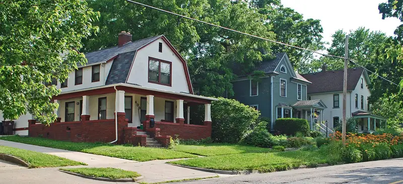 A brick bungalow and wood-frame houses under big trees
