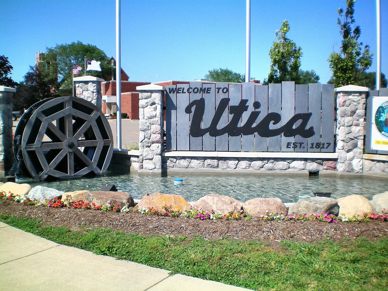 A stone welcome sign with a waterwheel and landscaping
