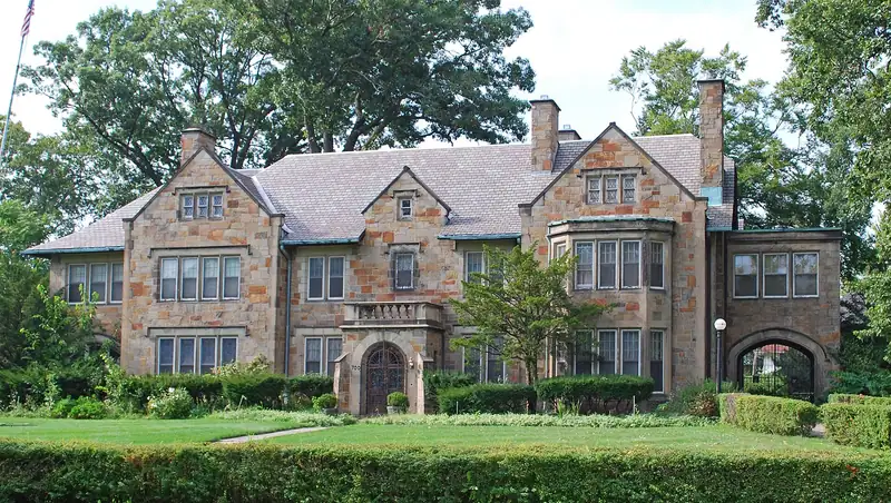 A stone and brick historic mansion behind trees