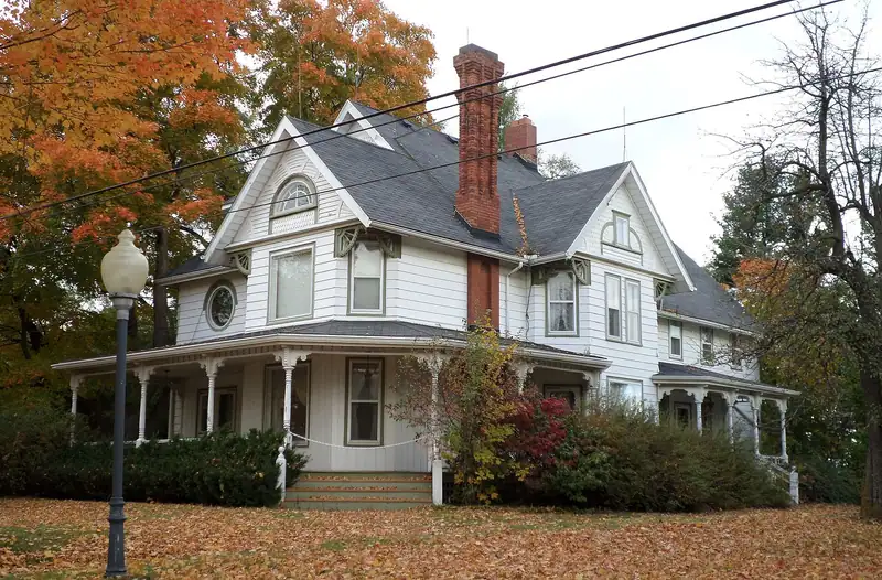A white Victorian house with a wraparound porch in the fall